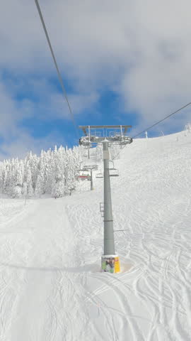 POV, TIMELAPSE, HYPERLAPSE: Scenic view of the ski resort while riding the chairlift up a crud snow slope. Chairlift ride over the tracked ski slopes towards the top of a mountain in the snowy winter.
