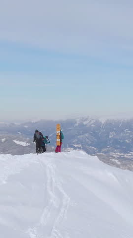 AERIAL: Flying around three ski tourers after reaching the snowy mountaintop overlooking the spectacular Slovenian countryside. Tourists observe the winter landscape before splitboarding down mountain