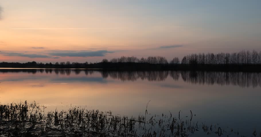 A wide lake at sunset at dusk, the darkening sky is reflected in the water of the lake at sunset, winter
