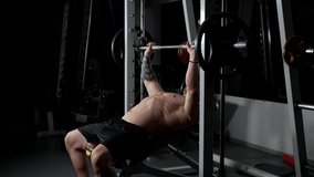 A muscular man with a bare chest is seen training in the gym with a barbell. He is performing bench press exercises using a Smith machine. The man lies on a bench and lifts weights. - Powered by Shutterstock - Get 15% off with code: PIKWIZARD15