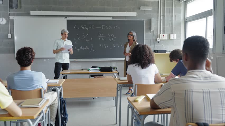 Male student reading a homework presentation to classmates and teacher at High School classroom