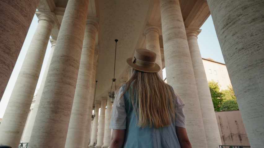 Young woman in a hat walking under the colonnade of St. Peter