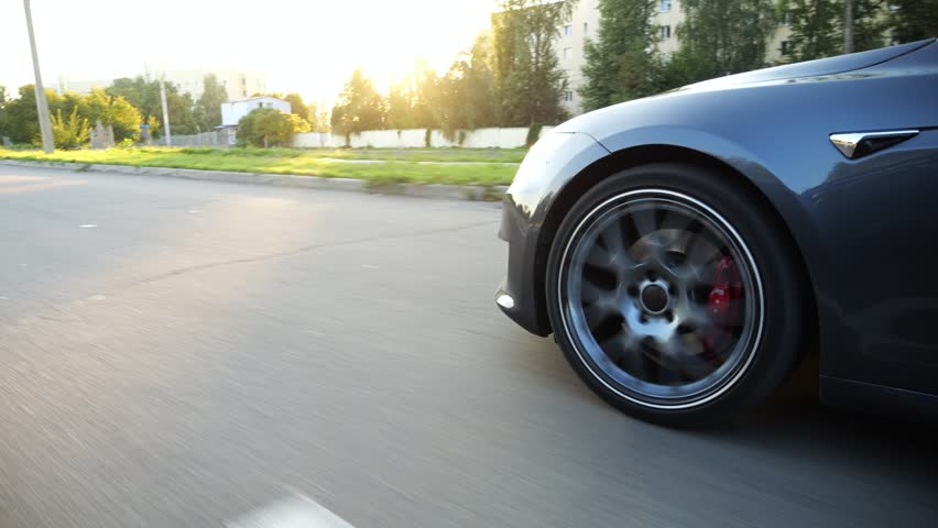 Wheel of modern electrical automobile driving at urban road on sunny day. Ecology friendly car riding moving along motorway. Electric vehicle riding through empty highway. Green innovation concept