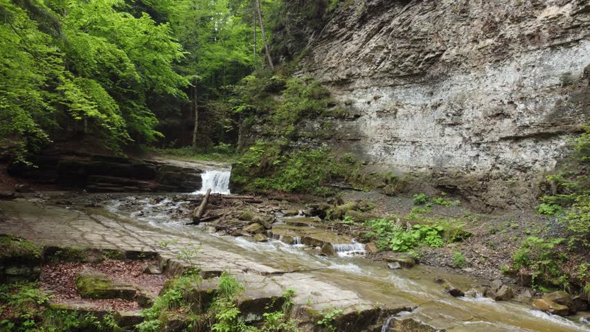 Maniavka river with two waterfalls on it in Ukrainian Carpathians, aerial view while moving backwards and down at overcast day
