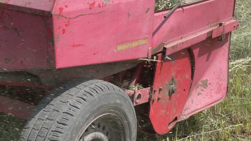 Baling of dried hay from the windrow in small rectangular bales bound with twine with small square baler towed by a tractor on a field in sunny morning
