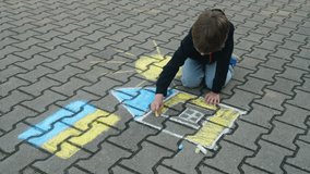 Child Draws With Chalk on Pavement Drawing of House, Sun and Ukrainian Flag. Little Boy Drawing Ukrainian Flag With Chalk. Crisis, Peace, Stop Aggression, Children Against War. Freedom to Ukraine. - Powered by Shutterstock - Get 15% off with code: PIKWIZARD15