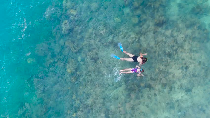 Aerial view of an adult woman and a young girl snorkeling with fins and masks in clear, shallow turquoise ocean water, Boracay, Philippines.