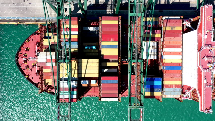 VALENCIA, SPAIN - AUGUST 14, 2025. Overhead aerial view of a giant container ship docked and downloading the containers by means of gantry cranes in the port of Valencia.