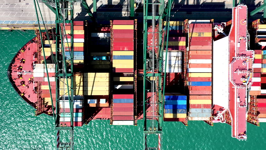 VALENCIA, SPAIN - AUGUST 14, 2025. Overhead aerial view of a giant container ship docked and downloading the containers by means of gantry cranes in the port of Valencia.