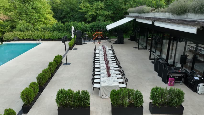 Beautiful outdoor venue featuring a long decorated table with grapes, a swimming pool, and lush greenery, perfect for weddings, parties, or corporate gatherings.