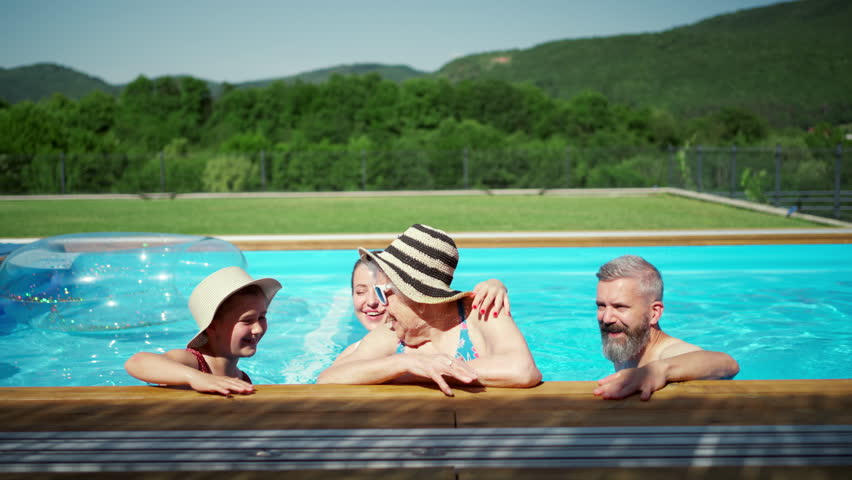 Multigenerational family enjoying summer time, sitting at backyard pool with legs in water.