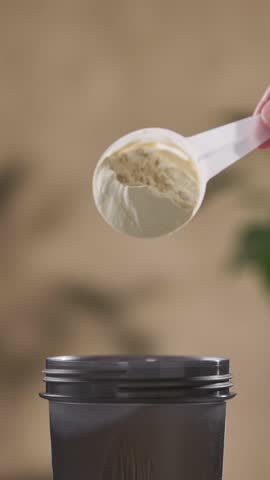 protein powder spills in cup from measure scoop.  whey sports nutrition. dry mixture for preparation of sporting or dietary drink.