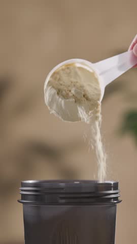 protein powder spills in cup from measure scoop.  whey sports nutrition. dry mixture for preparation of sporting or dietary drink.