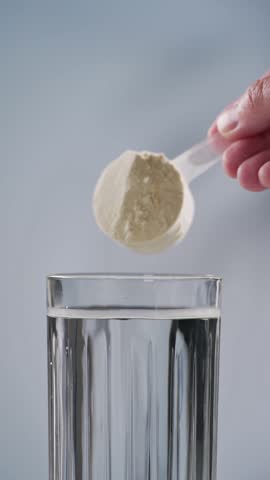 protein powder spills in glass of water from measure scoop.  whey sports nutrition. dry mixture for preparation of sporting or dietary drink.