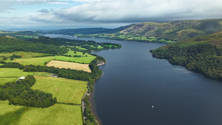 High angle drone view of Ullswater lake, green fields, and fells in Cumbria, UK