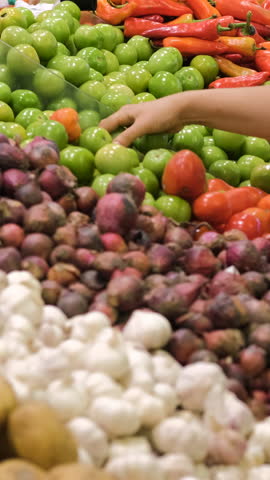 Vertical video. Woman selects green tomatoes in a fresh produce section of a grocery store, slow motion 
