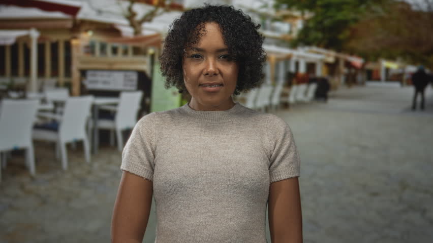 Woman standing with face framed wearing a beige sweater on terrace under natural light; quiet contemplation.