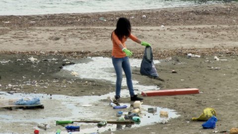Social worker woman with bag picking up garbage on sand in beautiful beach Stockvideó