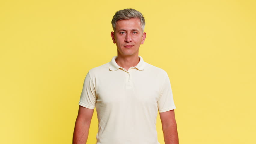 Middle-aged man smiling confidently and showing thumbs up as clear gesture of approval and agreement expressing trust and positivity. Guy demonstrating supportive emotion isolated on yellow background