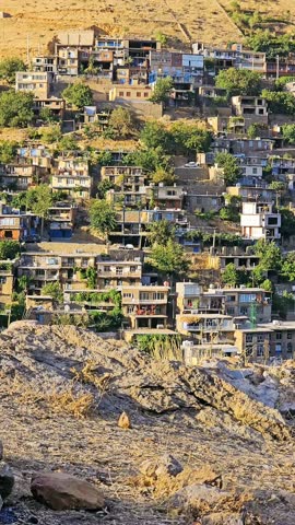 Kamalla stepped village in summer, built along a rocky hillside with tiered stone houses and contrasting greenery below, reflecting traditional adaptation to mountainous terrain.  
