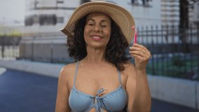 Woman outdoors in blue swimsuit holding pink razor smiling against urban street backdrop wearing sun hat during sunny day promoting summer shaving - Powered by Shutterstock - Get 15% off with code: PIKWIZARD15