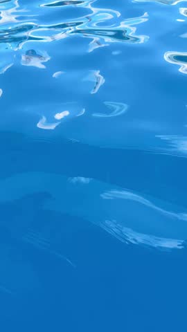 Calm blue water gently moves creating waves. Reflections of the afternoon sky and sunlight shimmer on the surface of the water