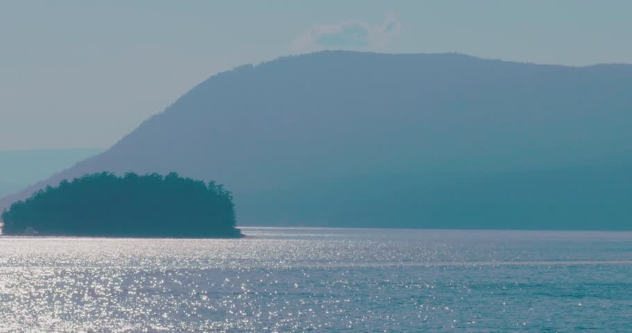Serene view of the shimmering Salish Sea with distant forested hills late afternoon. The Salish Sea stretches between Vancouver Island and the mainland of British Columbia, Canada