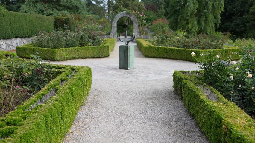 Sundial Sculpture in Formal Garden with Stone Pathways and Green Hedges in Summe