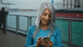 Senior woman with grey hair using phone on a cruise boat against seaside backdrop, enjoying a tranquil moment outdoors with a candid smile. - Powered by Shutterstock - Get 15% off with code: PIKWIZARD15