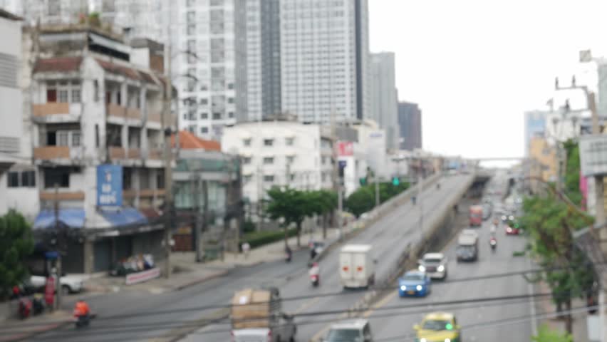Blurred daytime view of Bangkok street with moving traffic and vehicles.