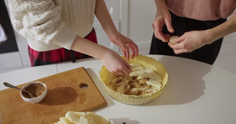 Teenage girl and her mother put filling on sliced apples while making sweet pie in cozy kitchen at home. Family Cooking and Baking at Home
