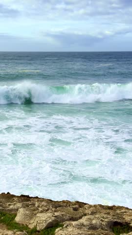 Powerful ocean waves crash onto rocky shores, beautiful day by seaside, tide of foam and spray. Bright sky, serene coastal atmosphere, natural beauty, moment of contemplation and quietness. 
