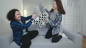 Couple enjoying a playful pillow fight on a cozy sofa in a well-lit living room during the afternoon - Powered by Shutterstock - Get 15% off with code: PIKWIZARD15