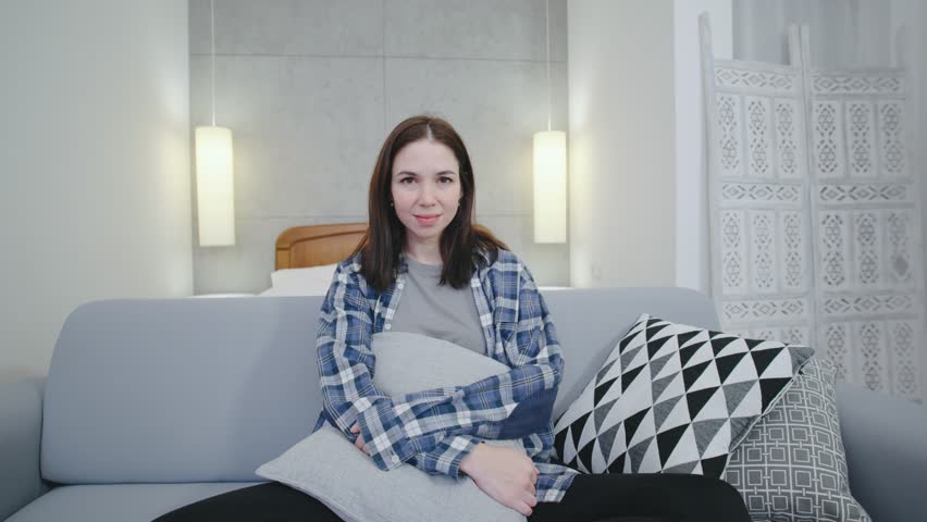 Young woman sits comfortably on a gray sofa in a cozy room during a relaxed afternoon at home