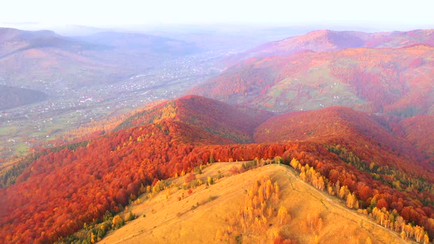 Stunning bird's eye view of a valley spread out among autumn hills in the golden light of dusk. Cinematic footage. Yaremche town, Carpathian, Ukraine. Filmed in UHD 4k. Discovery the beauty of earth.