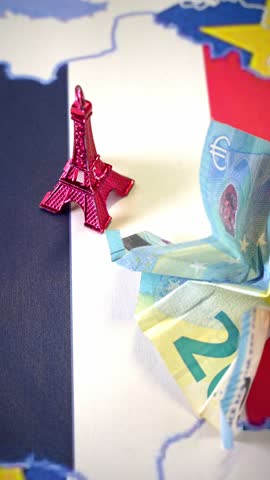 Eiffel Tower miniature and crumpled two euro banknote on France and European Union flag and map