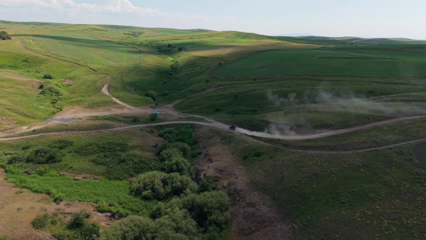 Green valley landscape featuring an off road vehicle kicking up dust as it navigates a winding dirt road, showcasing the thrill of adventure and exploration