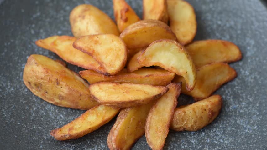 Grilled potato wedges with rosemary, cheese, salt and spices. Baked potato slices on a dark concrete background