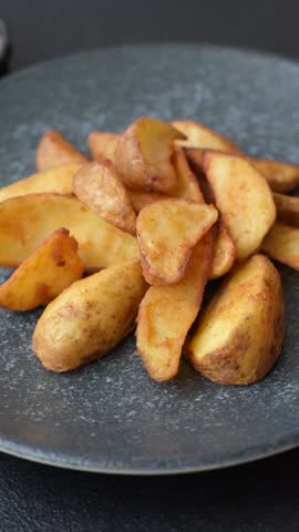 Grilled potato wedges with rosemary, cheese, salt and spices. Baked potato slices on a dark concrete background