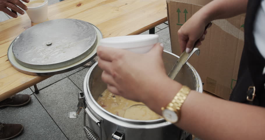 Serving traditional Polish pea soup (grochówka) from a field kitchen thermos during a public event. A person