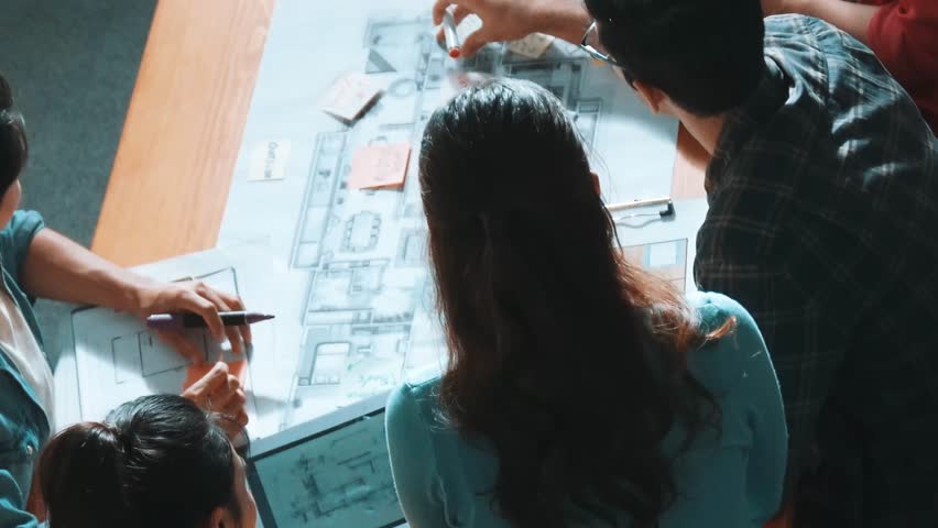 Top view of skilled civil engineer team writing at blueprint and planning design. Professional architect engineer working together sharing idea and taking a note in project plan at table. Symposium.
