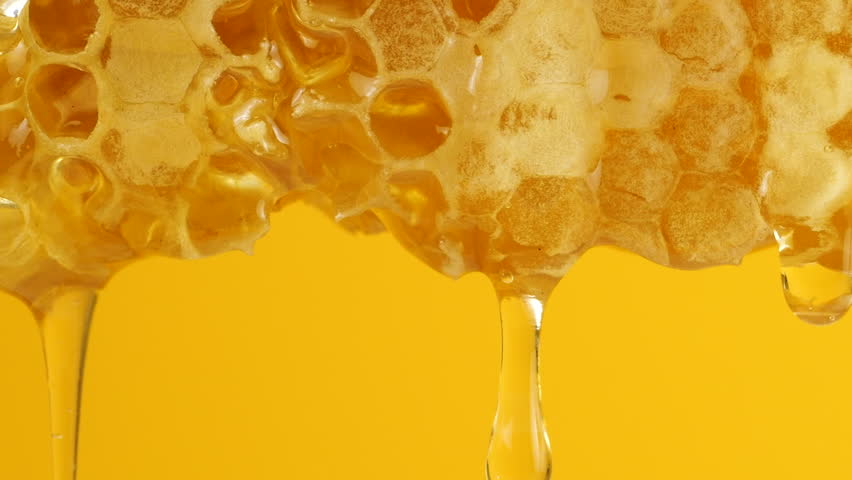 Golden honey drips from honeycombs against a yellow background. Close-up of wax honeycombs. Shooting macro. Healthy eating concept.