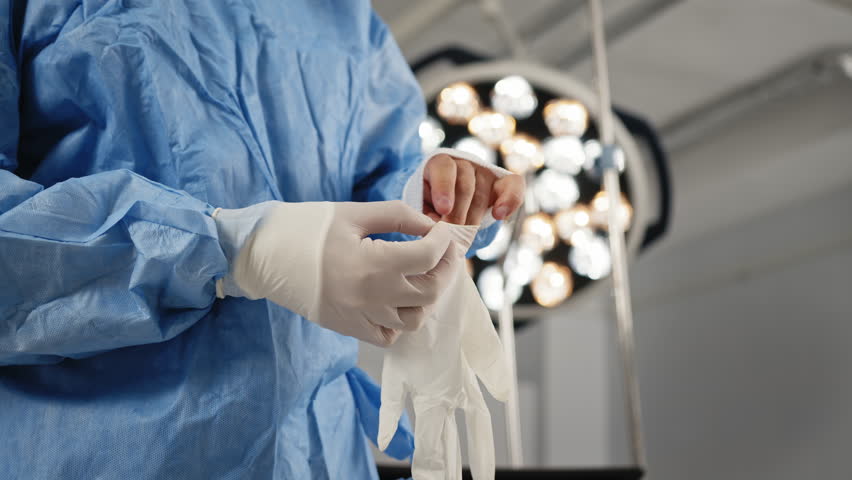 A medical professional putting on surgical gloves in an operating room, preparing for a procedure. A doctor, wearing a mask and surgical gown, stands in an operating room, preparing for a procedure. - Powered by Shutterstock - Get 15% off with code: PIKWIZARD15