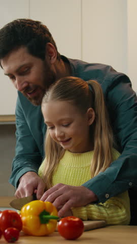 Family cooking together at home kitchen caring father helping teaching Caucasian kid daughter cutting cook vegetable salad dad with child girl preparing healthy food cut cucumber happy fatherhood