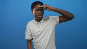 Young african american man with glasses shading eyes in blue studio wearing white polo shirt and trimmed afro haircut; anticipation curiosity exploration. - Powered by Shutterstock - Get 15% off with code: PIKWIZARD15