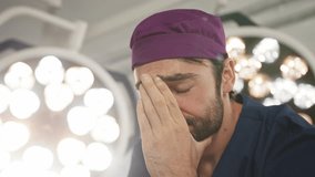 A somber, Caucasian male doctor in scrubs and a surgical cap, head in hands, perhaps experiencing distress. A concerned doctor in a surgical setting, illuminated by bright lights, expressing worry. - Powered by Shutterstock - Get 15% off with code: PIKWIZARD15