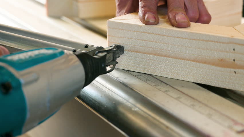 Close up view of a carpenter using a nail gun to nail a piece of wood. High quality 4k footage