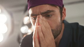 A surgeon takes a moment of reflection, his eyes closed, hand resting on his face. The doctor appears to be of Mediterranean descent. A concerned doctor in a surgical setting - Powered by Shutterstock - Get 15% off with code: PIKWIZARD15