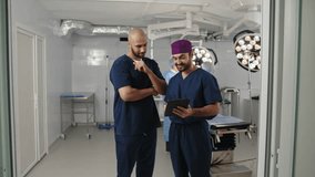 Two surgeons of Middle Eastern descent, dressed in scrubs, stand in an operating room. One looks at a tablet. Two surgeons of African and Middle Eastern descent reviewing - Powered by Shutterstock - Get 15% off with code: PIKWIZARD15