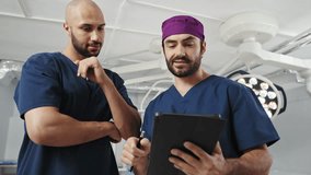 Two diverse doctors, one African-American and one Middle Eastern, collaborate in a bright hospital room, focused on a tablet. Surgeons in Operating Room - Powered by Shutterstock - Get 15% off with code: PIKWIZARD15